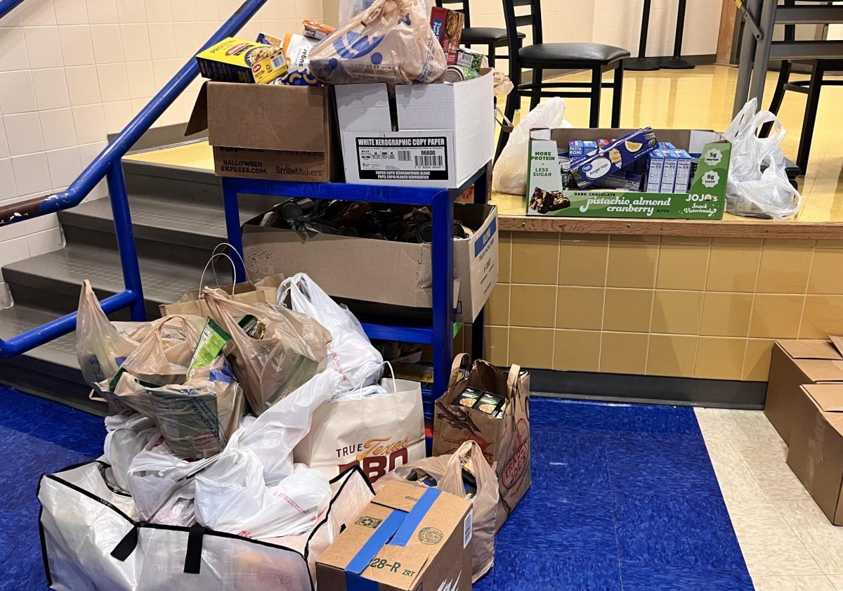Student donations to the food drive piled in front of the stage in the cafeteria. 